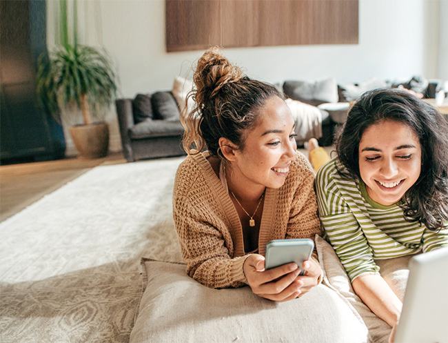 2 girls laying on a bed watching something on a laptop