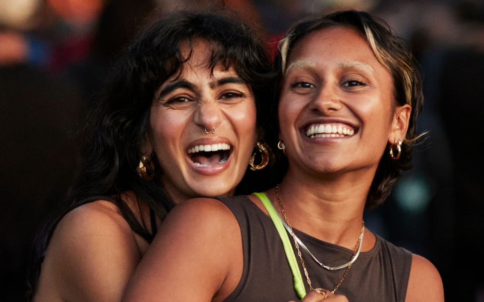 two girls smiling and laughing together at an outdoor event